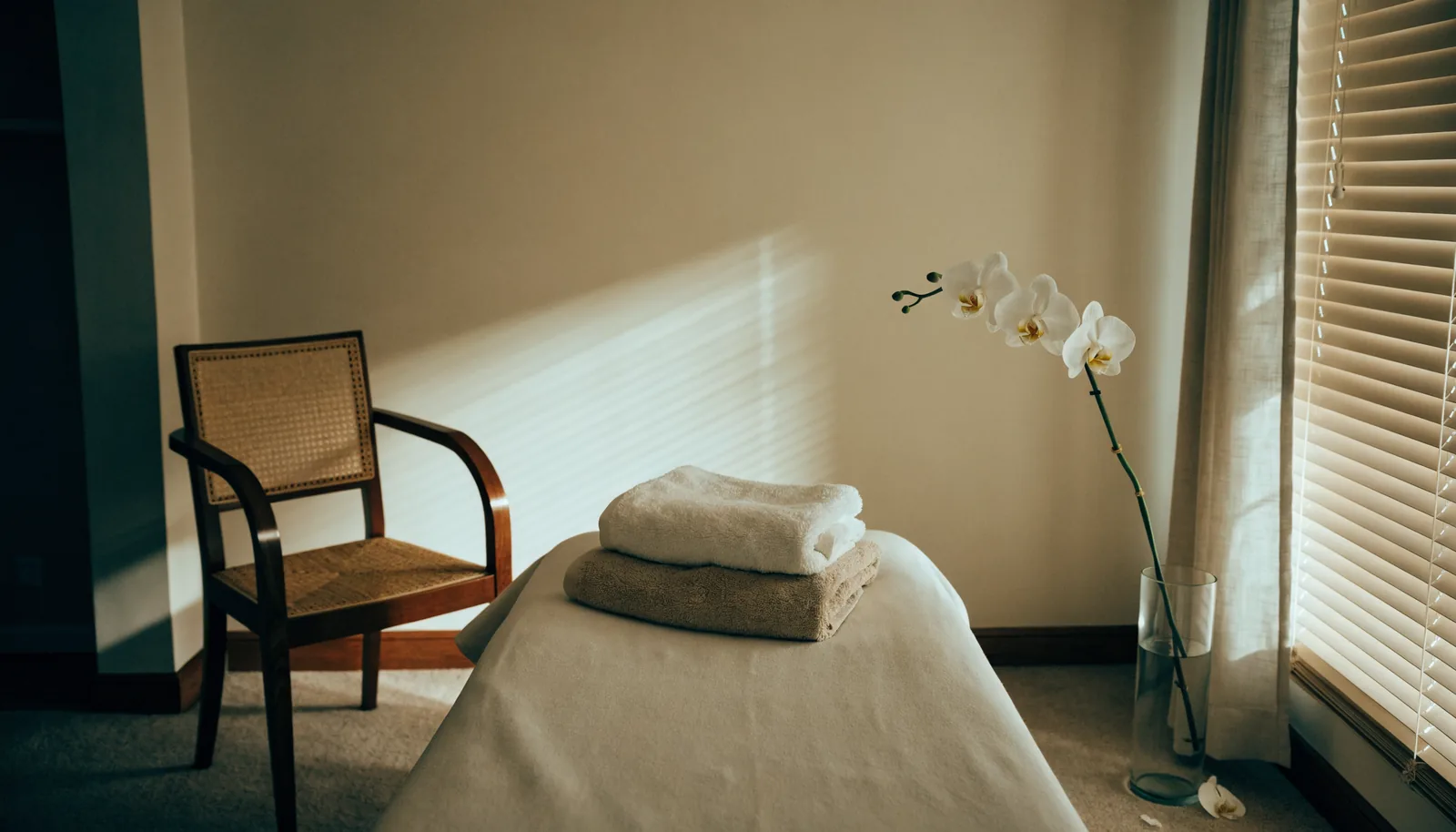 Empty spa treatment room with a made bed, folded towels and a fallen orchid petal